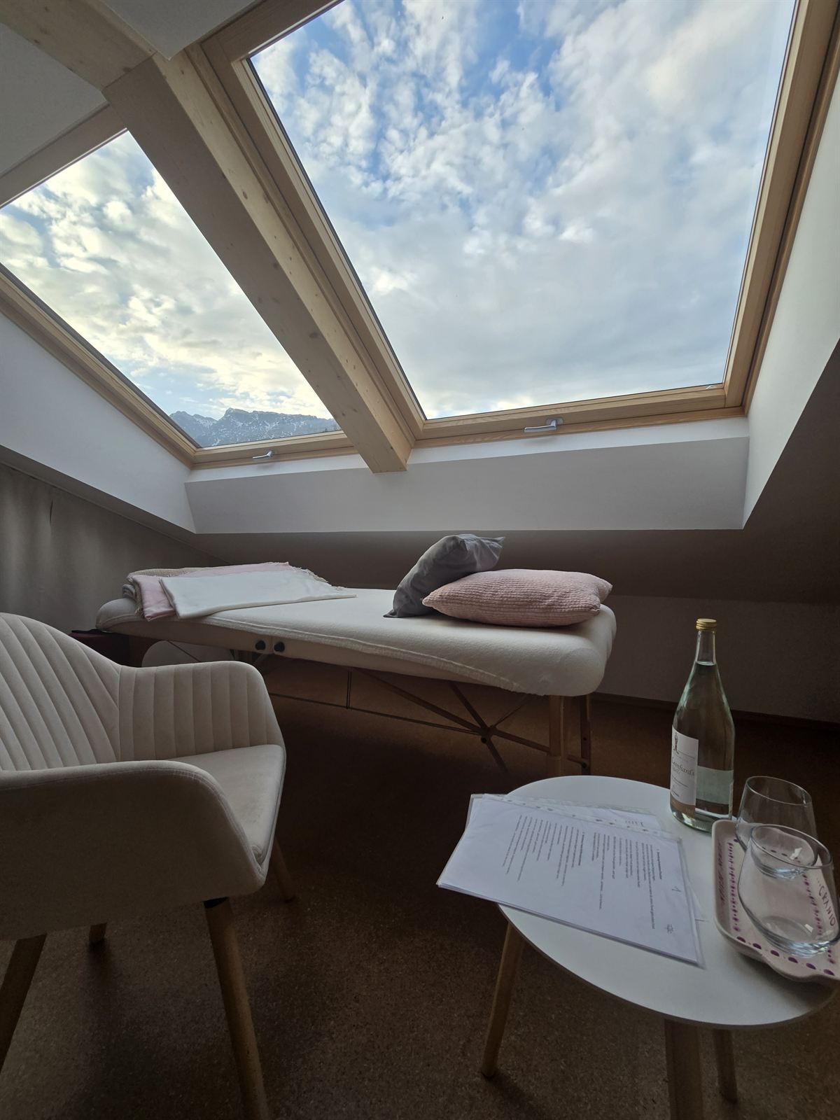 Behandlungsliege und Sessel im Studio unter den Dachfenstern, bereit für eine Sitzung